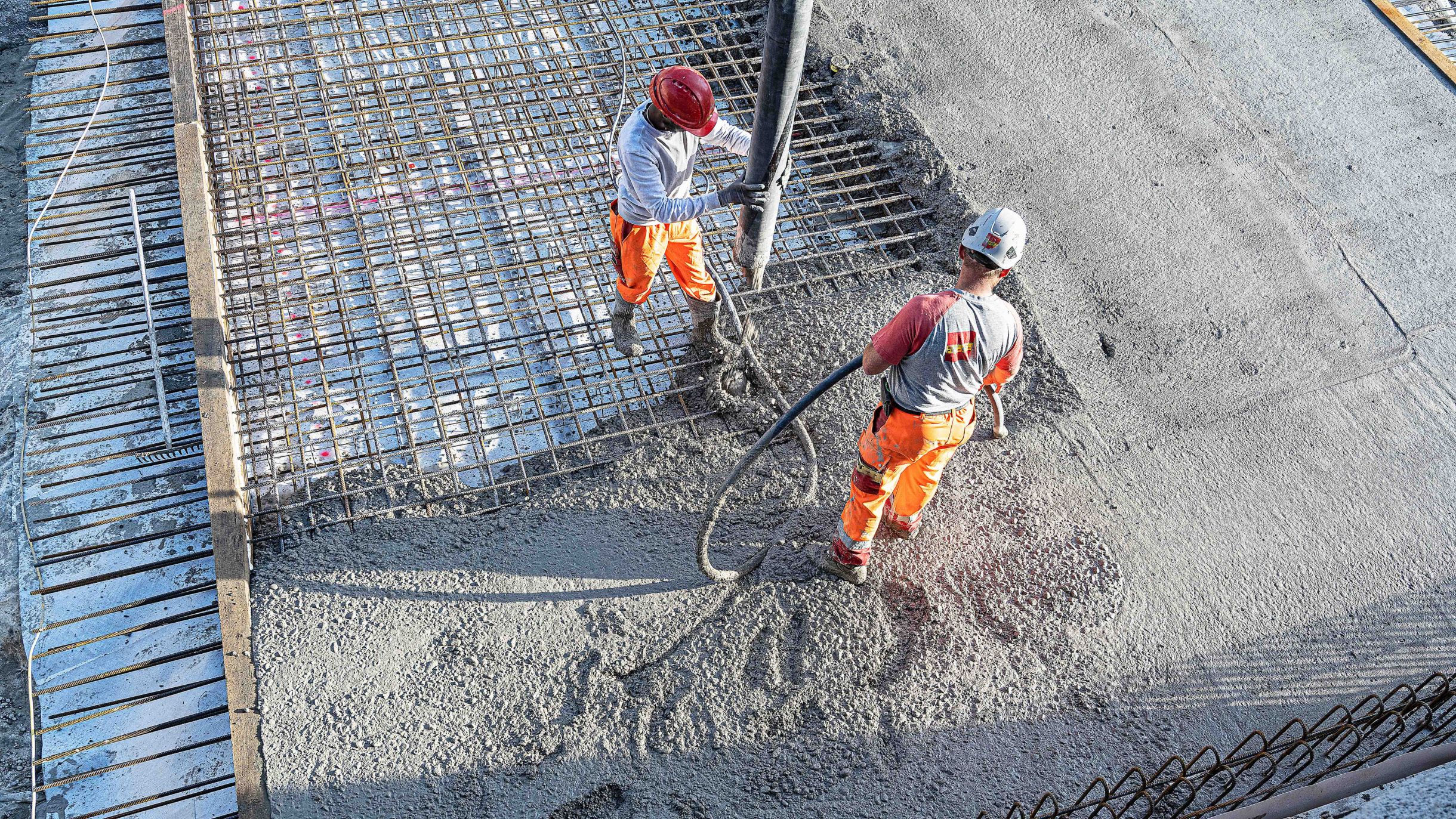 Two construction workers pouring cast-in-situ concrete onto reinforcement using a concrete pump