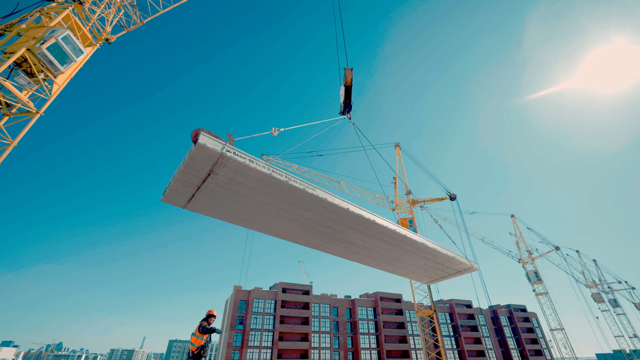 Crane lifting a precast concrete element (hollowcore slab) on a construction site in front of residential buildings