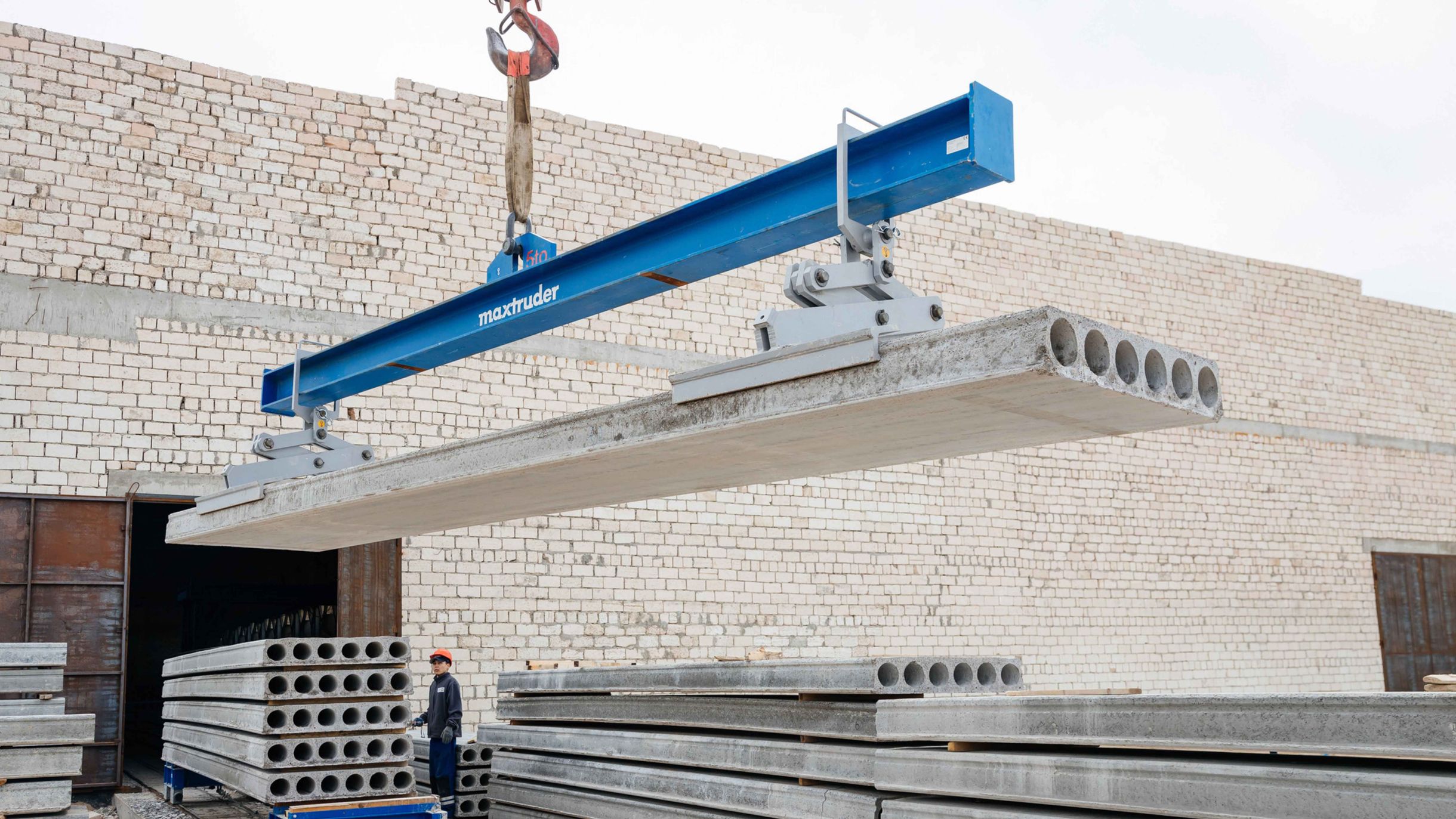 A hollowcore slab is being lifted by a crane using a blue lifting beam from the brand MAX-ruder.